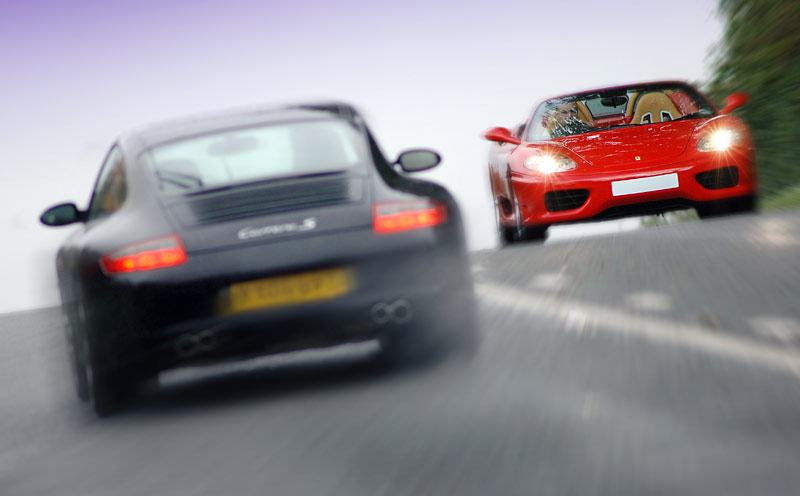 Porsche Carrera S rushing past a Ferrari 360 Spider on a minor Gloucestershire road.